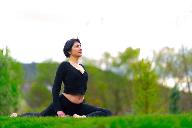 Mature woman doing yoga exercise with mat on grass in park