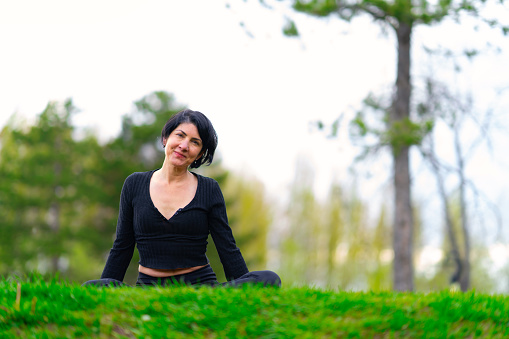 Smiling mature woman doing yoga exercise with mat on grass in park