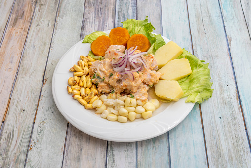 plate of fish ceviche marinated with lime and spices, with red onion, corn, boiled potatoes and cooked sweet potato on a white plate