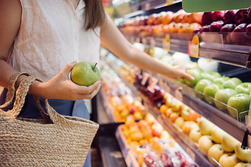 a woman holding a green apple for shopping in a grocery store, vegan lifestyle concept.