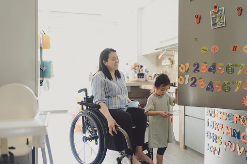 Beyond disability - Disabled Asian Chinese mother engages her 3 year old daughter in light household chores at the kitchen sink