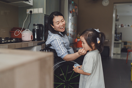 Beyond disability - Disabled Asian Chinese mother having fun with her 3 year old daughter while engaging in light household chores together