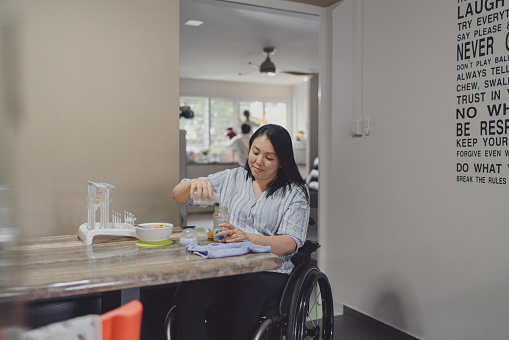 Cooking. A girl on a wheelchair opening oven in the kitchen while cooking soemthing