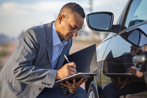 Insurance agent inspecting a car with a scratch and taking notes.