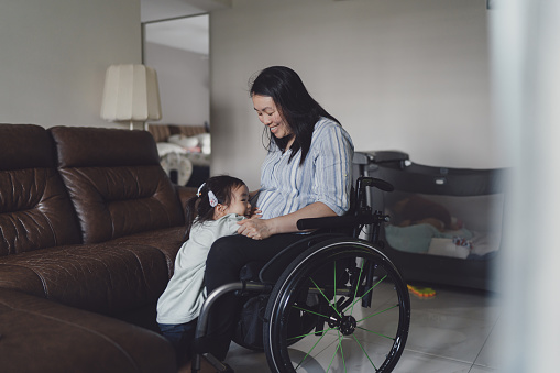Beyond disability - Asian Chinese mother in a wheelchair looking after her two young kids at home