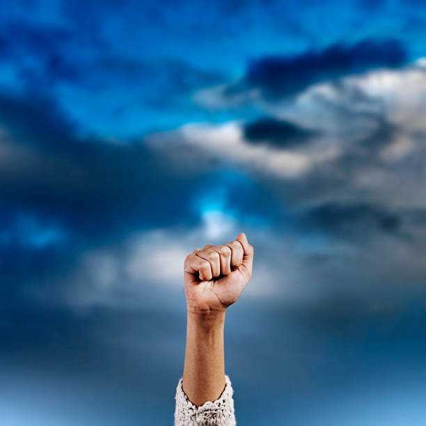 istock Woman's clenched fist raised against a dramatic story sky with copy space 1491743014
