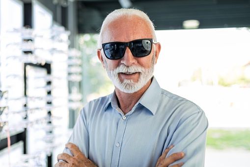 Senior man choosing wearing sunglasses in optical store