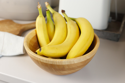 Bunch of bananas in a wooden bowl on a kitchen counter.