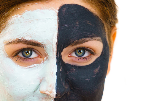 Woman with clay carbo black mask on half face and white mud on second half. Girl taking care of oily complexion. Beauty procedures. Skincare.