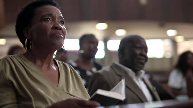 Senior woman holding open Bible listening to preacher in church service