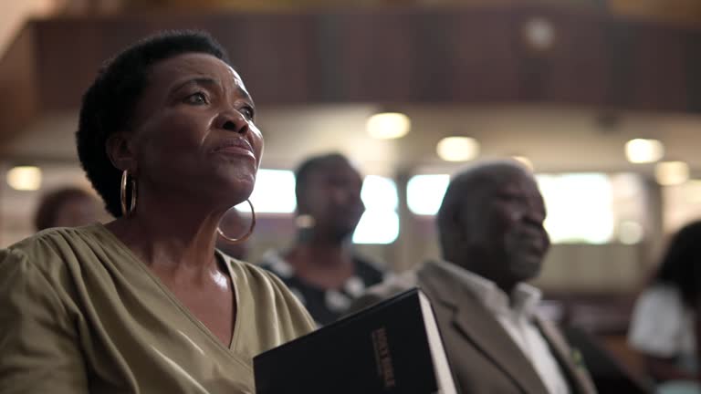 Senior woman holding open Bible listening to preacher in church service