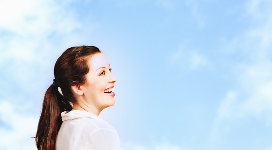 Attractive young woman smiles against a beautiful summer sky.