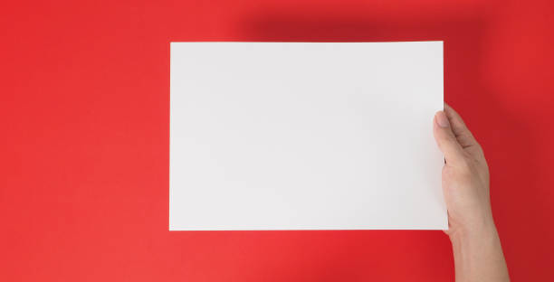 istock One hand is holding blank white A4 paper on red background. 1491755129
