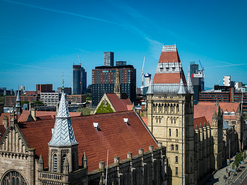 An aerial photograph of Manchester University Rooftop’s on Oxford Road in Manchester, England. The photograph was taken on a bright sunny day with clear blue skies. The skyline of downtown Manchester skyline can be seen in the distance