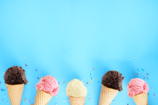 Ice cream bottom border over a blue background. Dark chocolate, pink strawberry and white vanilla flavors. Copy space.