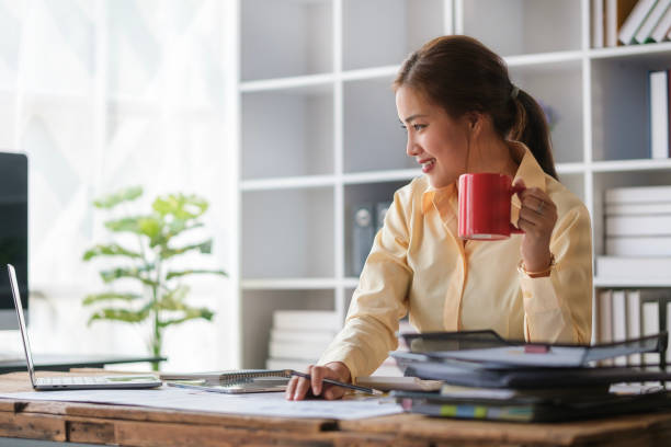 istock Attractive female analyst drinking coffee and using laptop computer in bright office. 1491760260