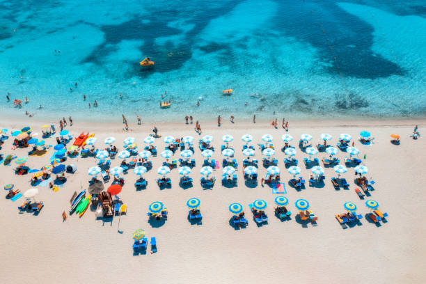 Aerial view of colorful umbrellas on sandy beach, swimming people in blue sea at summer sunny day. Sardinia, Italy. Tropical seascape. Travel and vacation. Top drone view of ocean with azure water stock photo