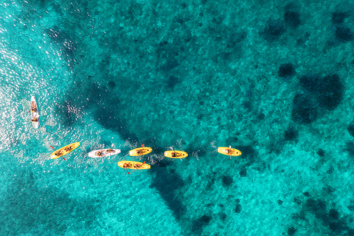 Aerial view of yellow kayaks in blue sea at summer sunny day. People on floating canoes in clear azure water. Sardinia island, Italy. Tropical landscape. Sup boards. Active travel. Top view from drone