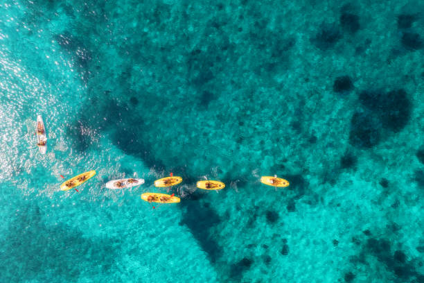 Aerial view of yellow kayaks in blue sea at summer sunny day. People on floating canoes in clear azure water. Sardinia island, Italy. Tropical landscape. Sup boards. Active travel. Top view from drone stock photo