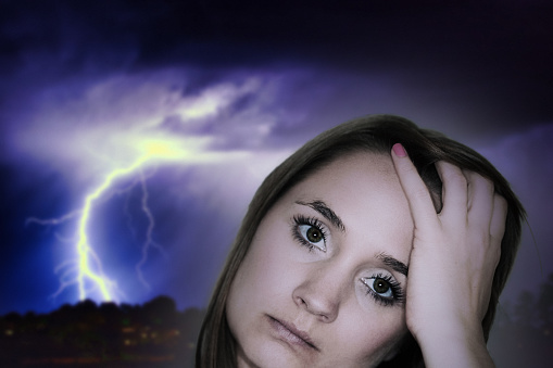 Trouble woman's face in close-up with lightning striking behind her.