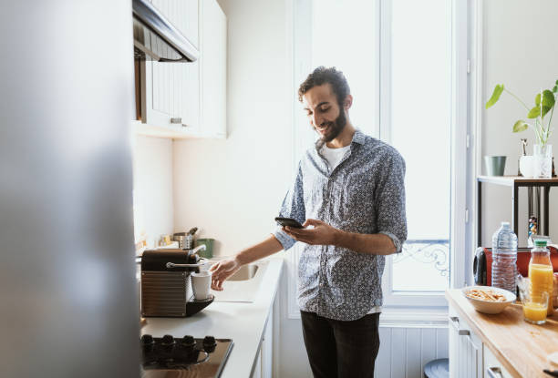 istock Mid adult multiracial man preparing coffee at home and using smart phone 1491764908