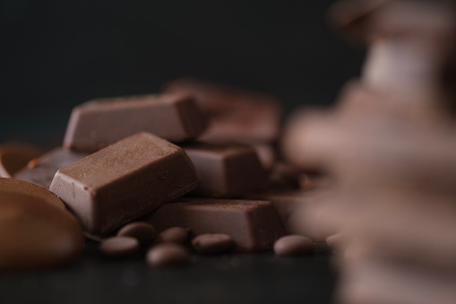 Closeup shot of chocolate cubes and chocolate chips on black background. Dessert food background.