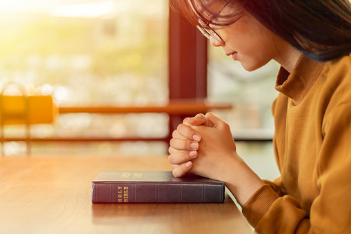 Young Asian Woman Hands folded in prayer on a Holy Bible.