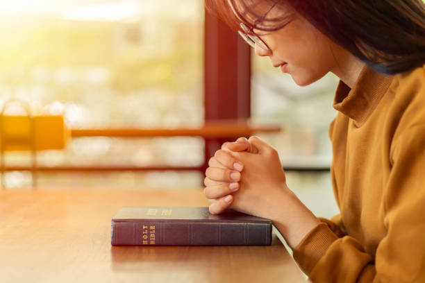 young asian woman hands folded in prayer on a holy bible. - prayer call imagens e fotografias de stock