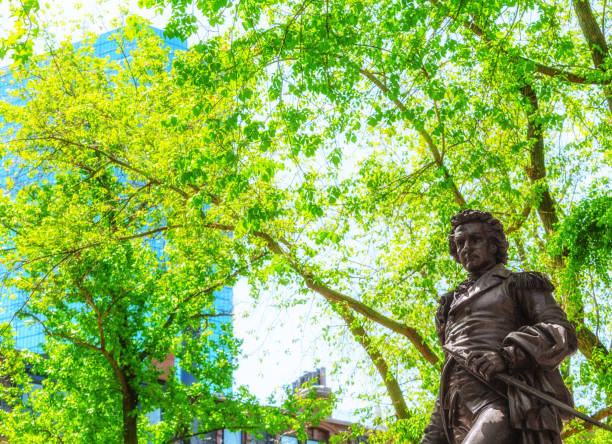 Boston, Massachusetts, USA - May 17, 2023: A statue of John Glover is installed on the Commonwealth Avenue Mall, between Berkeley and Clarendon Streets in Boston's Back Bay neighborhood. John Glover (1732 - 1797) was a Revolutionary War hero who helped Washington cross the Delaware and whose brigade helped give the Marines their name. Martin Milmore sculpted the piece in 1875. John Hancock skyscraper in the background.
