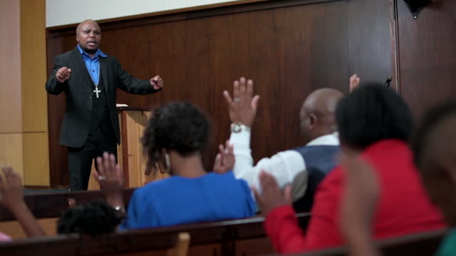 Over shoulder view to preacher as congregation raises hands in prayer