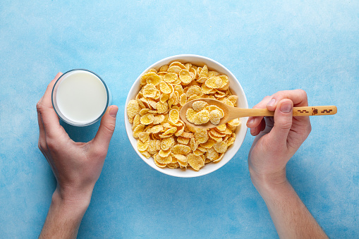 Yellow corn flakes and a glass of milk for dry breakfast. Top view. Cereals spoon and bowl