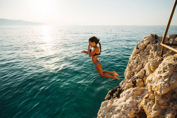 istock Side view of a young girl jumping from a cliff 1491779246