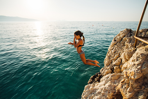 Side view of a young girl jumping from a cliff on her summer vacation