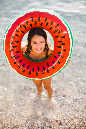 Smiling girl holding inflatable ring and standing on the beach