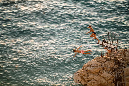 Teenagers having fun jumping from a cliff in to the sea