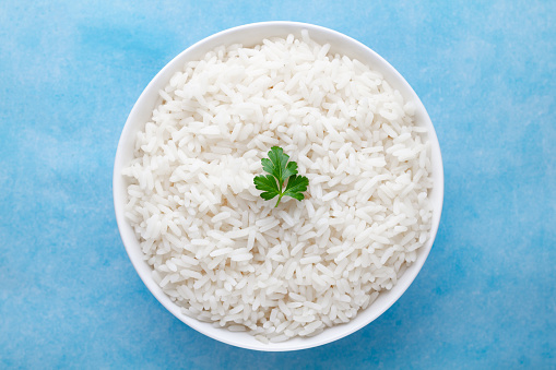 Bowl with white boiled rice with green fresh parsley for delicious healthy lunch on a blue background. Cereal food and dishes. Top view