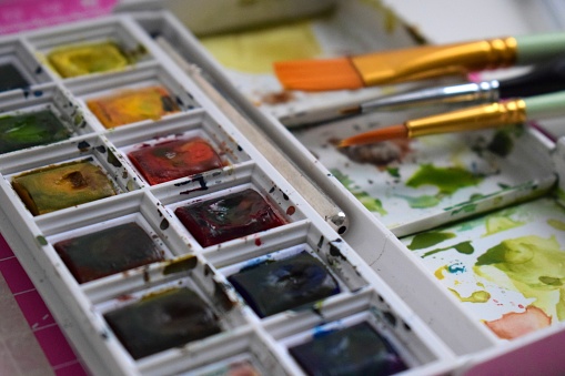 Close up of a used watercolour paint palette with professional paint brushes.