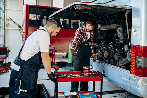 Two young adult bus mechanics working in a repair station garage. Automotive industry and service concept.