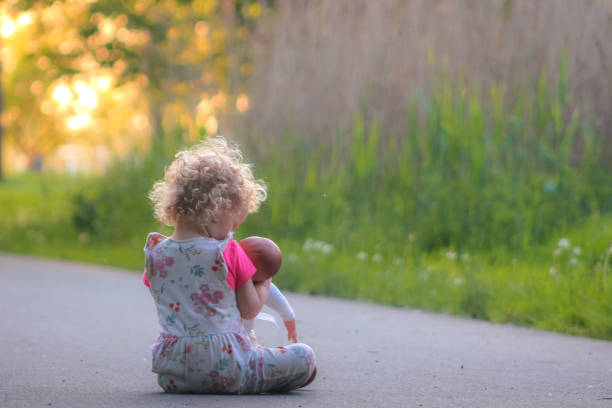 Blond, curly girl sitting on a park path, holding her doll