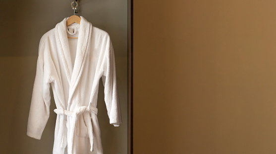 Hanger with clean white bathrobe in hotel wardrobe. Space for text