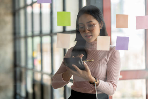 istock Businesswoman using calculator and post-it note on glass wall to calculate and write strategic business plan to develop success. 1491794119