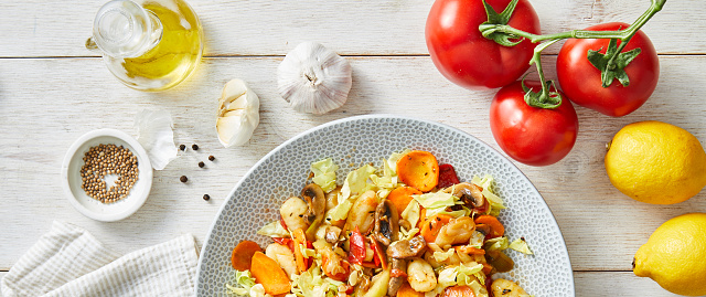 Delicious homemade spring vegan gnocchi with fresh vegetables. carrot, red pepper, zucchini, served on a modern ceramic plate, with seasoning and herbs on a white rustic wooden kitchen or restaurant table, representing a healthy lifestyle, wellbeing and body care, top view with a copy space