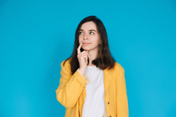 thoughtful and stylish woman in trendy clothing - portrait of an attractive young lady with a skeptical gaze, isolated on blue background - copy space available - bolero jacket imagens e fotografias de stock