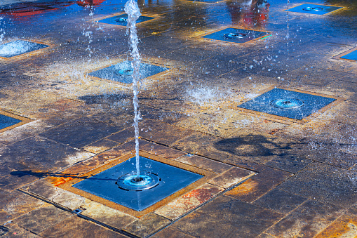 Splashing water fountain on the pavement . City summer wet street