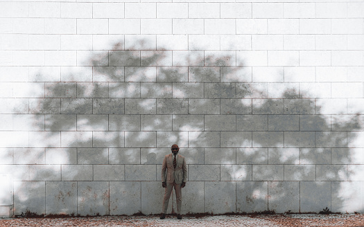 Lisbon; a black man standing elegantly and serenely in front of a white tile wall texture background, wearing a cream suit. A shadow of a big tree is showing on him and the wall behind him