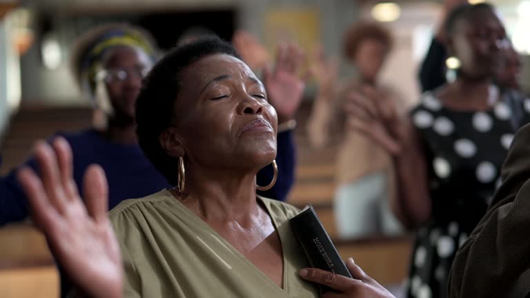 Senior woman with eyes closed and hand raised praying in church