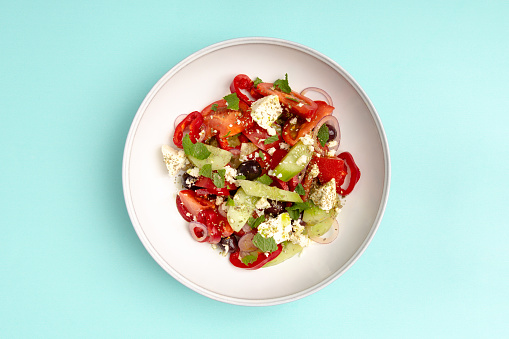Plate with salad with tomato, cucumber, pepper, onion, feta cheese and olive on blue background