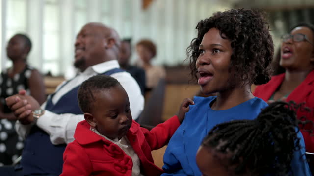 Woman sitting in church with baby and family giving praise listening to preacher