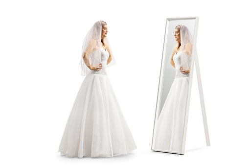 Full length profile shot of a bride standing in front of a mirror isolated on white background