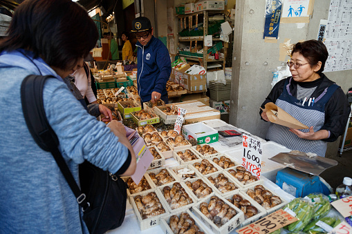 Tokyo, Japan - May 21, 2023 : japanese senior woman selling fresh matsutake mushroom to customer to cook famous delicious food in autumn at vegetable stall at tsukiji fish market in Tokyo, Japan.